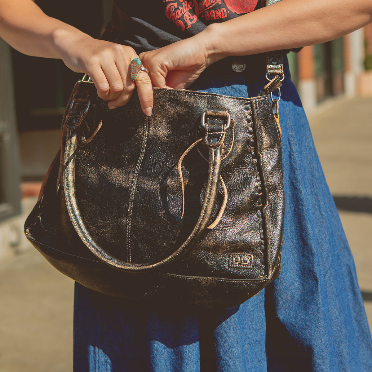 Person holding a stylish, practical Bed Stu Rockababy bag while standing on a sunny street.