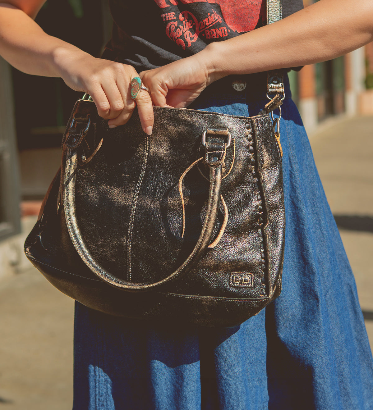 Person holding a stylish, practical Bed Stu Rockababy bag while standing on a sunny street.