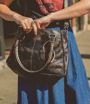 Person holding a stylish, practical Bed Stu Rockababy bag while standing on a sunny street.