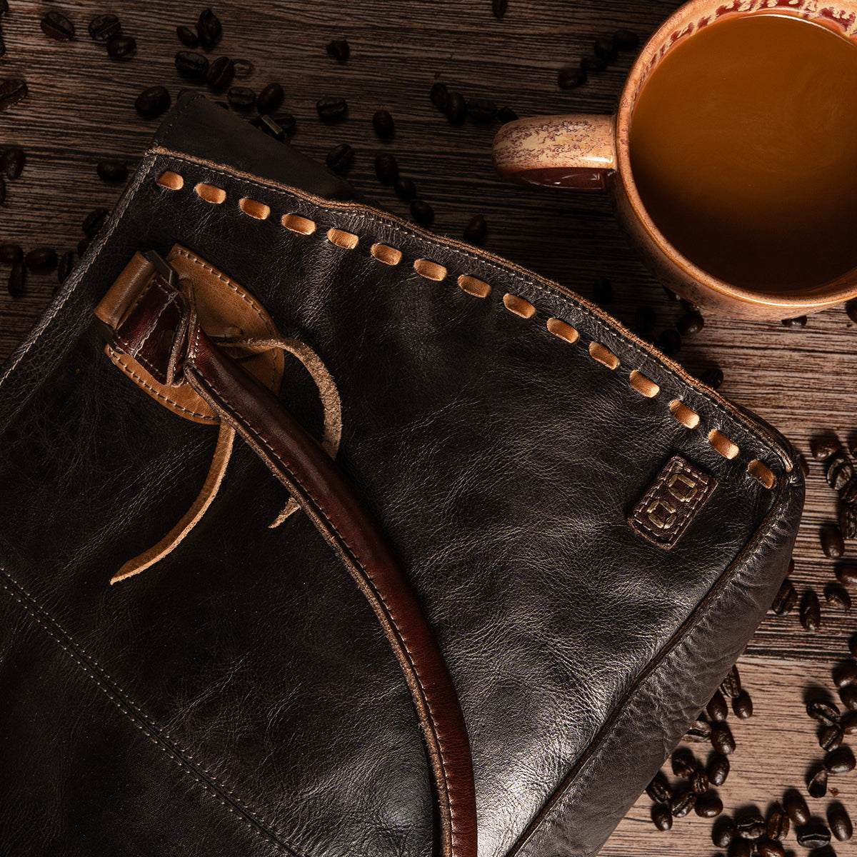 Rockababy compact vegetable-tanned leather bag with woven edge detail, next to a mug of coffee and scattered coffee beans on a wooden surface.