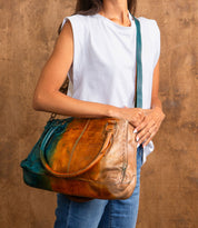 A person in a white sleeveless top and blue jeans holds the large Bed Stu Rockababy bag with padded shoulder straps against a brown background.