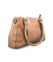 A tan leather Bed Stu Rockababy bag with double handles, decorative stitching, and a crossbody strap is displayed on a plain white background.