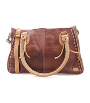 The Bed Stu Rockababy is a handcrafted brown full-grain leather handbag with tan handles, decorative stitching, a shoulder strap, and side details, shown on a white background.