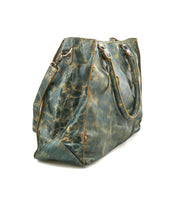The Bed Stu Rockaway is a distressed green leather tote bag with double handles, side straps, and a zip-pocket divider showing visible wear. Photographed on a white background, this best-seller blends style and function.