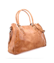 The Bed Stu Rockaway is a tan leather handbag featuring two handles and a versatile shoulder strap. It has stitched details, metal rings, and a zip-pocket divider on a clean white background.