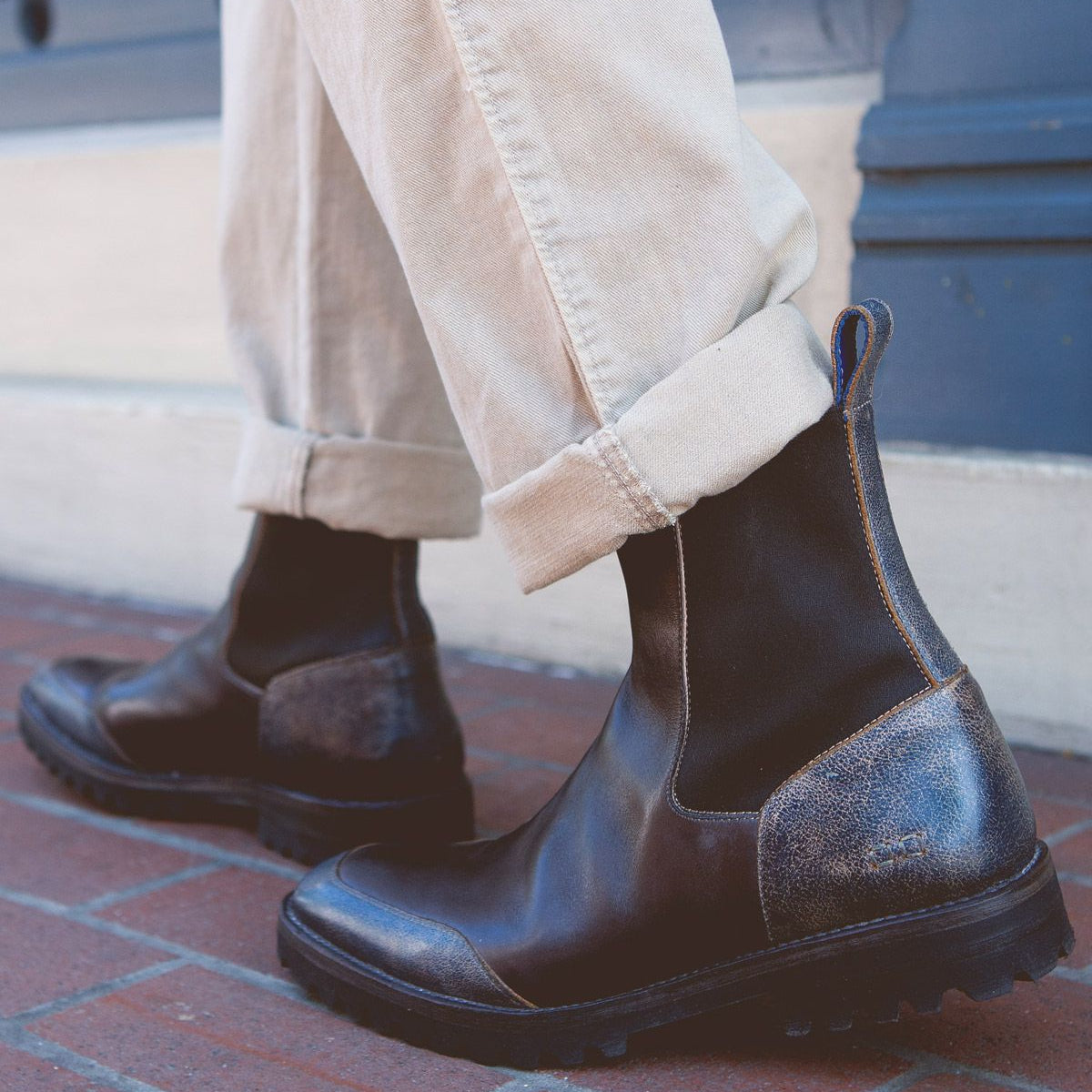 A person wearing the Bed Stu Salatiel, exuding timeless style with their brown leather finish and unmatched comfort, paired with rolled-up beige pants on a brick sidewalk.