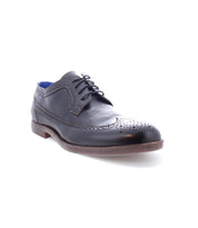 The Sandro II by Bed Stu is a handcrafted black leather men's office shoe, boasting exquisite brogue details and a wingtip toe. It features laces, decorative perforations, and a contrasting brown sole against a pristine white background.