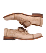Pair of beige lace-up handmade Sandstorm derby shoes by Bed Stu with brown soles, featuring a suede upper, placed side by side facing opposite directions on a white background.