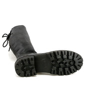 The Bed Stu Scope is a tall black women’s leather boot, shown lying on its side to highlight the boot’s rugged tread pattern.