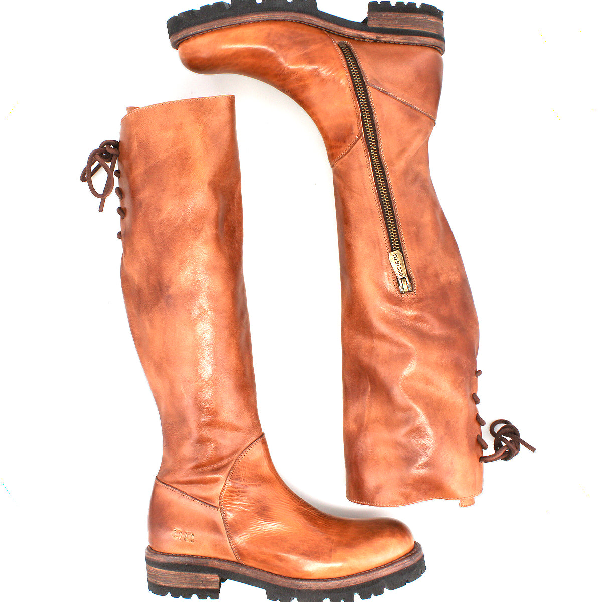 The Bed Stu Scope boots are tall women’s boots made from vegetable-tanned leather, featuring side zippers, a lace-up back, and rugged rubber soles—shown with one boot upright and the other laid horizontally.