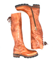 The Bed Stu Scope boots are tall women’s boots made from vegetable-tanned leather, featuring side zippers, a lace-up back, and rugged rubber soles—shown with one boot upright and the other laid horizontally.