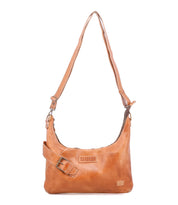 The Bed Stu Seemly is a compact tan leather shoulder bag featuring an adjustable strap, decorative buckle, and a front logo patch—ideal for everyday style.