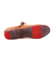 A brown leather Shuffle III with red rubber patches on the sole, featuring an adjustable buckle strap by Bed Stu. Embracing the ballerinacore trend, this design captures a modern yet timeless aesthetic. The sole shows visible wear, adding character to its chic style.