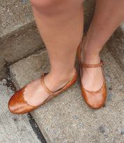 Close-up of a person's feet wearing Bed Stu Shuffle III brown leather Mary Jane shoes with an adjustable strap, standing on concrete steps.
