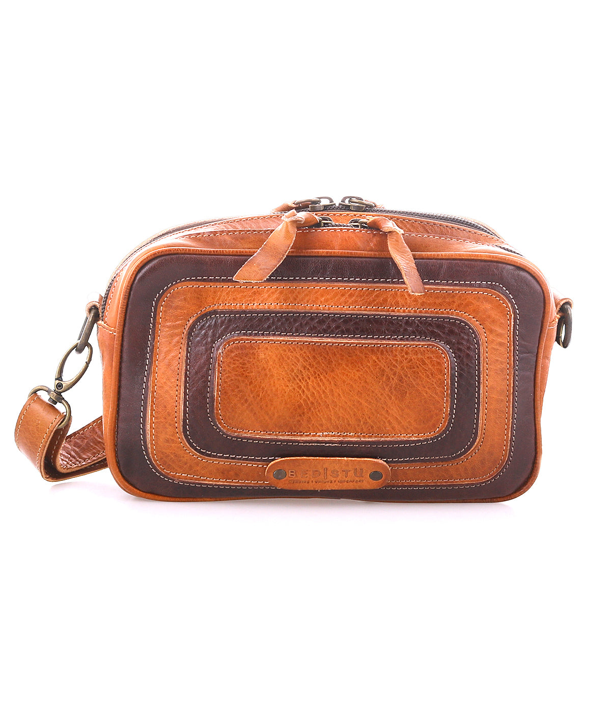 The Bed Stu Shy is a compact rectangular brown leather crossbody with a long strap, double zipper closures, and stylish layered leather details on the front.