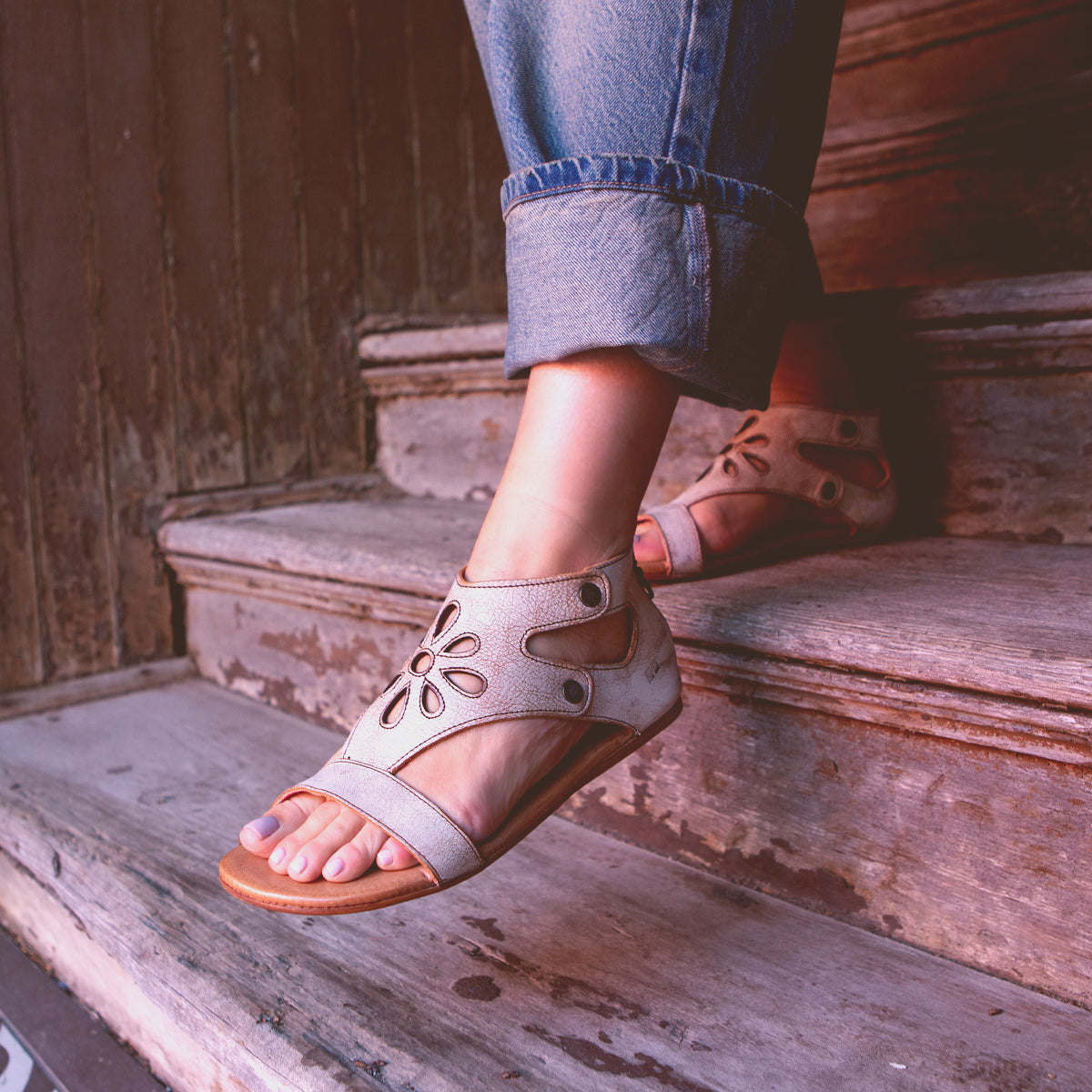A person wearing Bed Stu Soto Cutout sandals resting their feet on wooden steps.