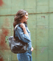 A woman exuding vintage-chic sophistication with her Stevie jeans and a black leather tote from Bed Stu, showcasing the impeccable craftsmanship.