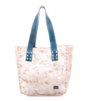 The Stevie by Bed Stu is a beige leather tote bag featuring visible stitching, blue leather handles, and a small rectangular metal logo on the lower front—ideal for everyday use.