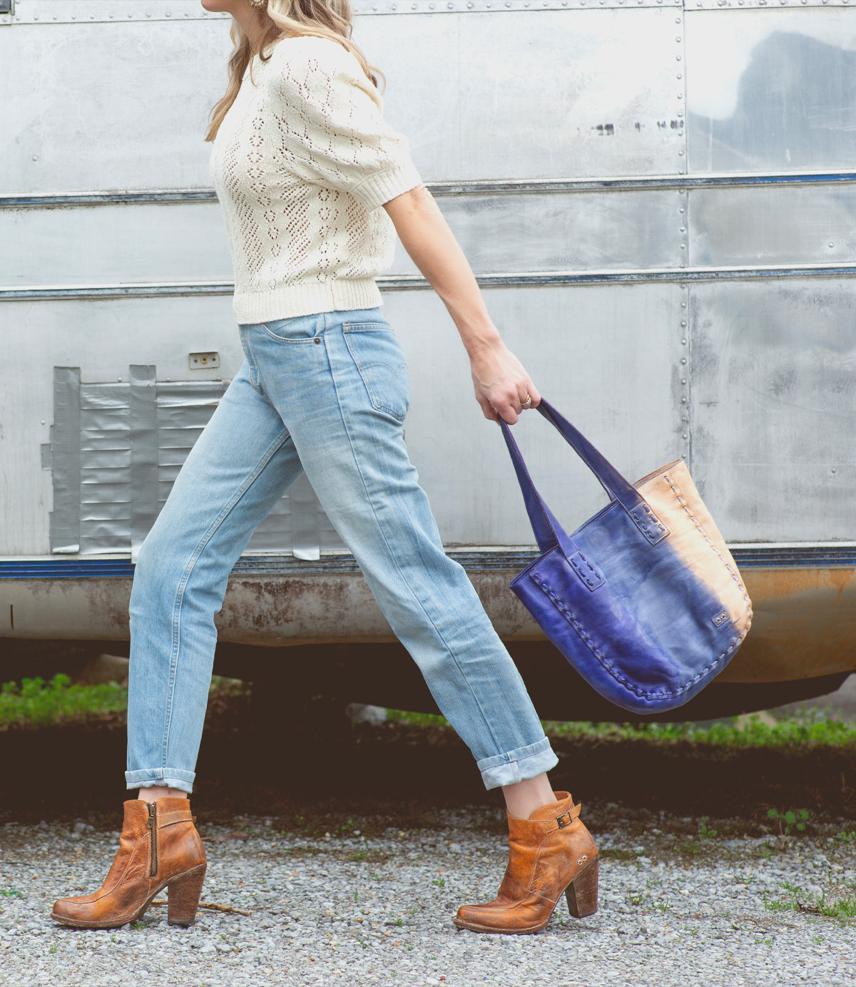 A woman walking with a blue Bed Stu Stevie modern tote in front of a trailer.