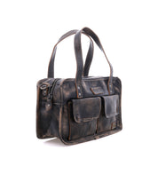 The Bed|Stü Stuffy handbag, crafted from brown distressed leather, boasts dual handles, a structured silhouette, two front flap pockets, a zipper closure, and a spacious interior, shown against a white background.