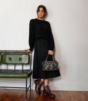 A woman in a black sweater, black skirt, and brown lace-up leather boots carrying a Bed|Stü Stuffy, a distressed leather handbag with a structured silhouette and spacious interior.