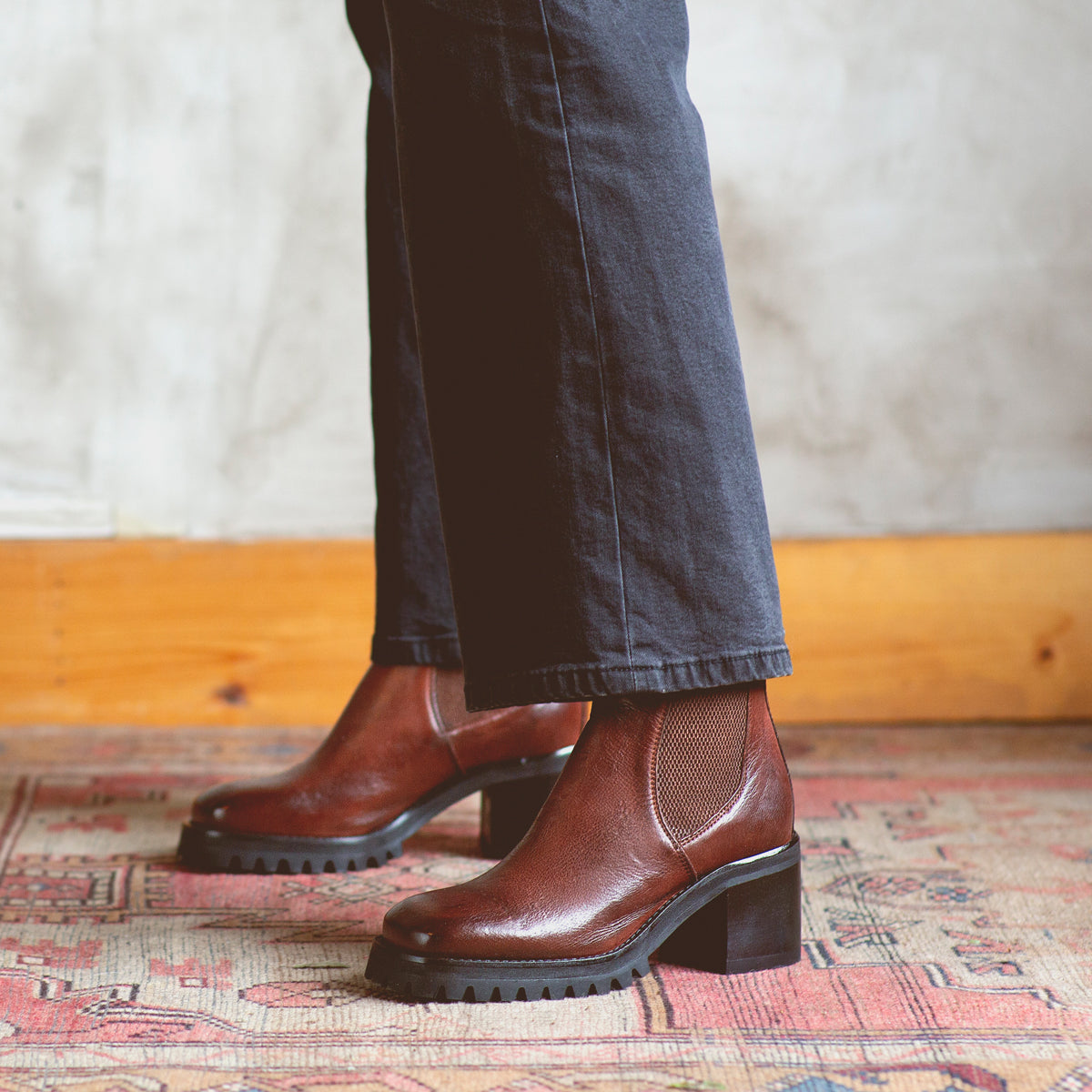 A woman is standing on a Surge rug wearing a pair of Bed Stu Chelsea boots made of Italian leather.