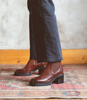 A woman is standing on a Surge rug wearing a pair of Bed Stu Chelsea boots made of Italian leather.