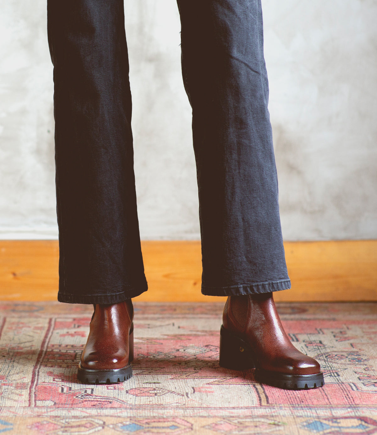 A woman wearing jeans and Bed Stu Chelsea boots on a rug.