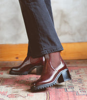 A woman wearing Bed Stu Surge Italian leather Chelsea boots with a higher heel on a rug.