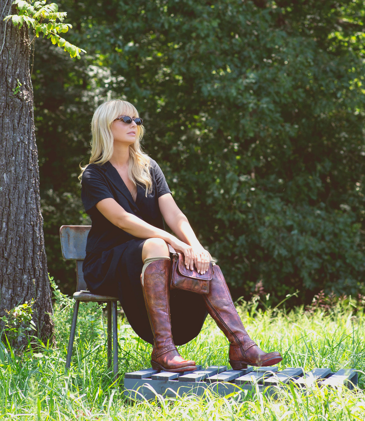 A woman in Takoma by Bed Stu, a western-shaped heel, is sitting on a bench in a field with leather inlays.