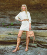 A blonde woman in brown boots is posing for a photo with the Bed Stu Takoma, featuring a western-shaped heel.