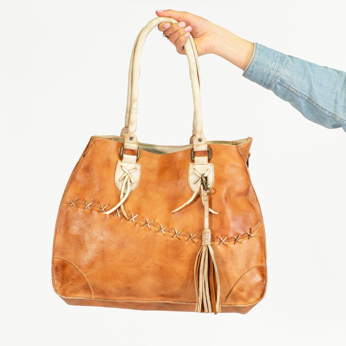 An accessory with tassels, the Bed Stu brown leather bag is being held by a hand, showcasing personal expression.