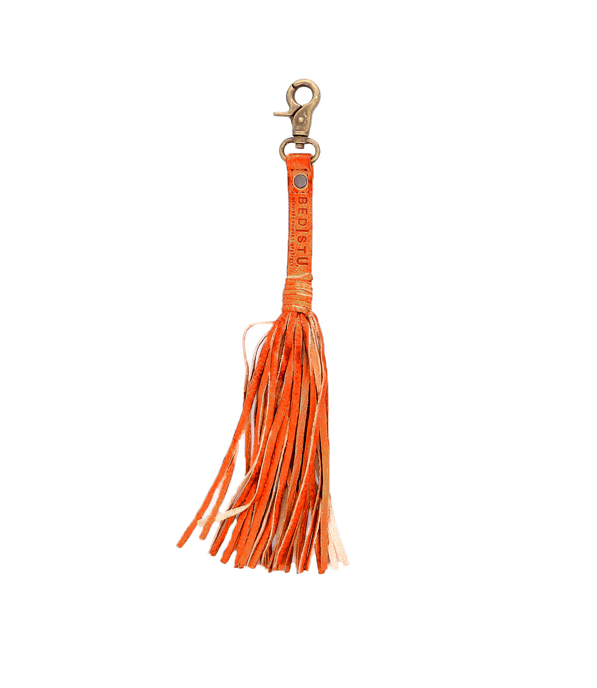 The Bed Stu Tassel Clip is an orange leather keychain with a metal clasp, made from premium leather. It includes long, thin strips and stamped text on the handle, adding versatility to any ensemble.