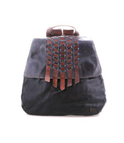 The Bed Stu Teji is a black leather statement backpack with a flap featuring brown leather woven detailing, shown against a white background.
