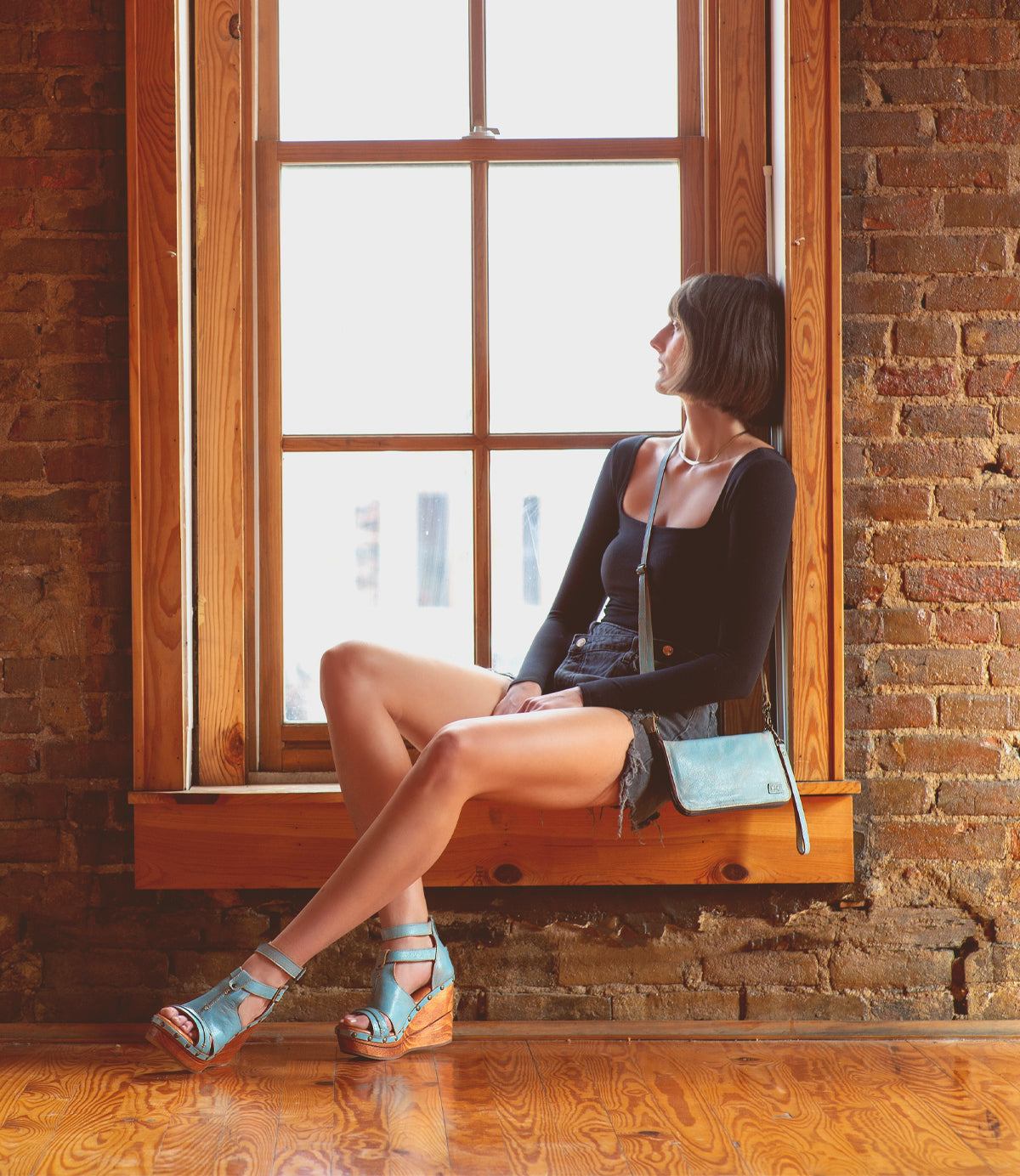 A woman sitting on a window sill, clutching a Bed Stu Templeton II leather wallet.
