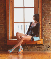 A woman sitting on a window sill, clutching a Bed Stu Templeton II leather wallet.