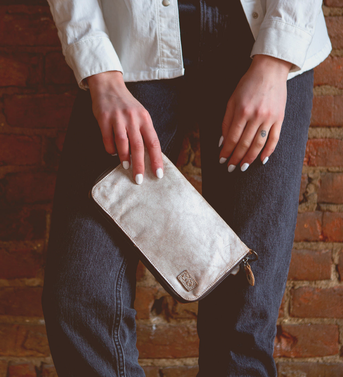 A woman holding a white leather Templeton II wallet against a brick wall.