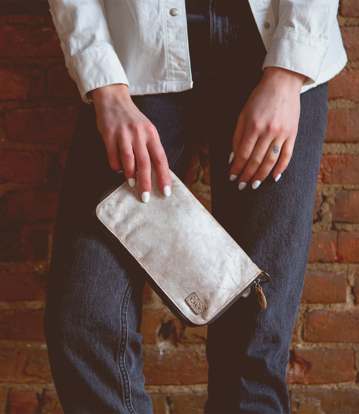 A woman holding a white leather Templeton II wallet against a brick wall.