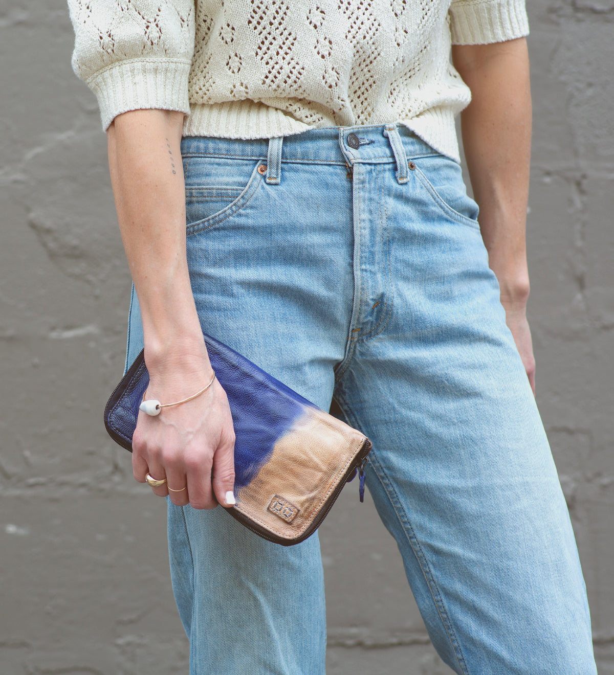 A woman wearing jeans and a sweater holding a Bed Stu Templeton II leather wallet.