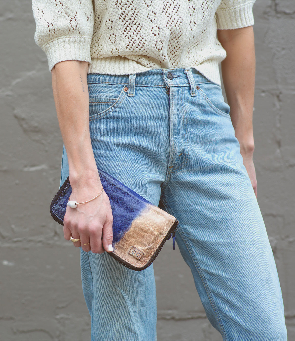 A woman wearing jeans and a sweater holding a Bed Stu Templeton II leather wallet.
