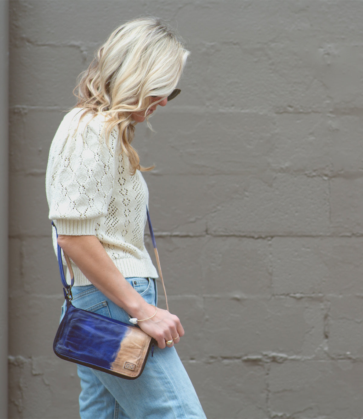 A blonde woman wearing jeans and a Bed Stu Templeton II leather wallet crossbody with a blue purse.