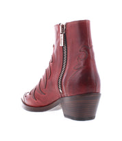 The Bed Stu Tentativa is a red leather ankle boot featuring artisan details, decorative stitching, a side zipper, and a stacked low heel, shown from the back on a white background.