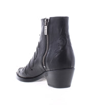 The Bed Stu Tentativa is a handcrafted black leather ankle boot with a side zipper, low heel, and decorative stitching, displayed from a rear side angle on a white background.