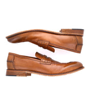 A versatile pair of brown leather penny loafers, viewed from the side, with visible stitching and slightly worn soles, handcrafted in Italy – The Time by Bed Stu.