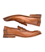 A versatile pair of brown leather penny loafers, viewed from the side, with visible stitching and slightly worn soles, handcrafted in Italy – The Time by Bed Stu.