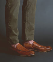 A person wearing olive green pants and handcrafted brown leather Bed Stu Time loafers stands against a dark background, exuding sophistication.