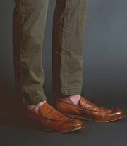 A person wearing olive green pants and handcrafted brown leather Bed Stu Time loafers stands against a dark background, exuding sophistication.