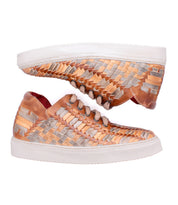 The Bed Stu Unwavering sneakers, featuring handwoven leather with copper and silver metallic strips, white soles, and laces, are displayed side by side on a white background to highlight their unique dimensional pattern.