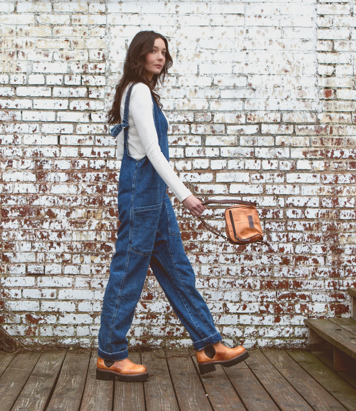 A woman wearing Bed Stu Valda Hi overalls and carrying a bag.