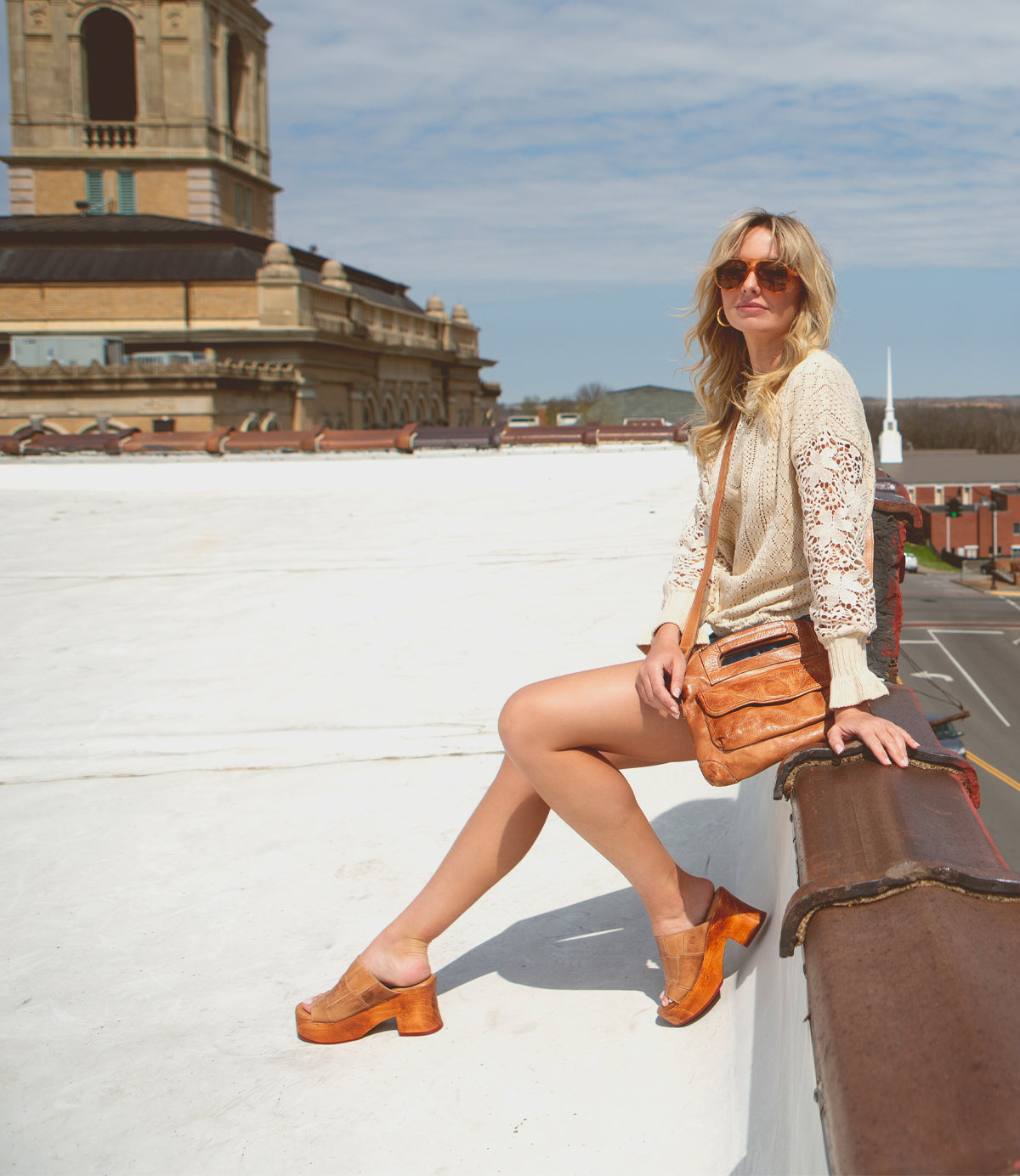 Woman sitting on a Bed Stu Vanquish platform with a cityscape background on a sunny day.